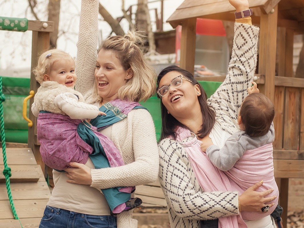 Two happy mothers in a park with babies in baby carriers wrap